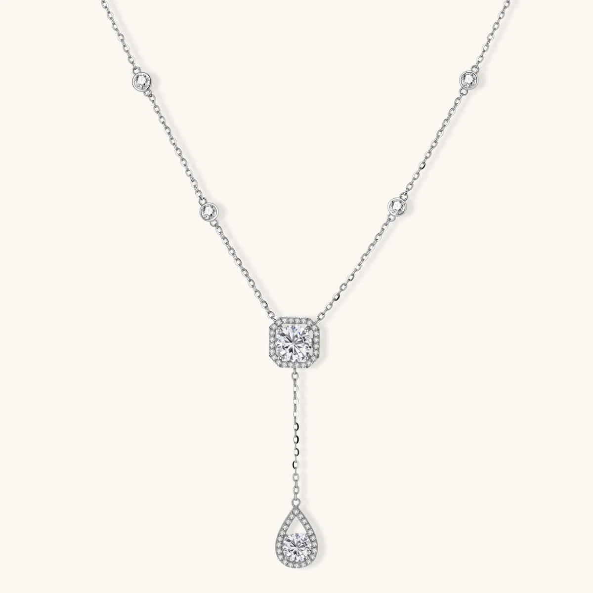 Sterling silver necklace with cushion-cut moissanite in halo setting and teardrop pendant, displayed on cream background.