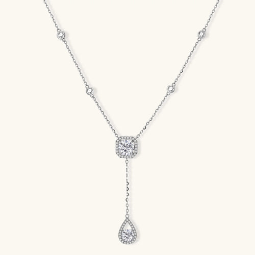 Sterling silver necklace with cushion-cut moissanite in halo setting and teardrop pendant, displayed on cream background.