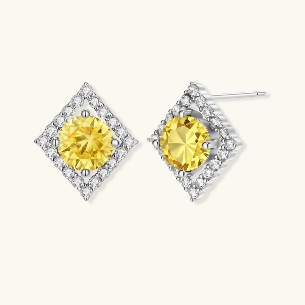 Close-up of diamond-shaped stud earrings with yellow moissanite centers and clear stone halos in sterling silver setting