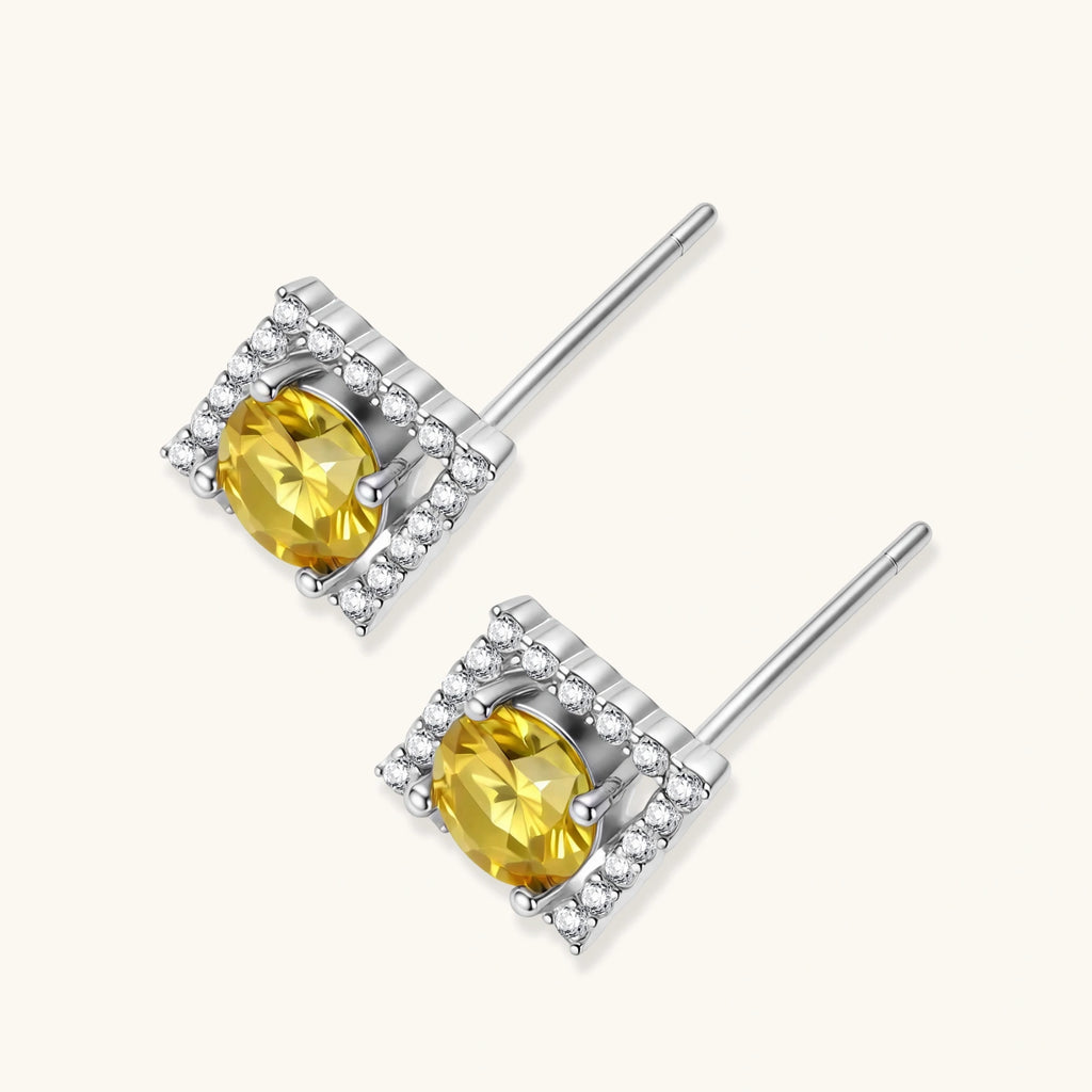 Close-up of diamond-shaped stud earrings with yellow moissanite centers and clear stone halos in sterling silver setting