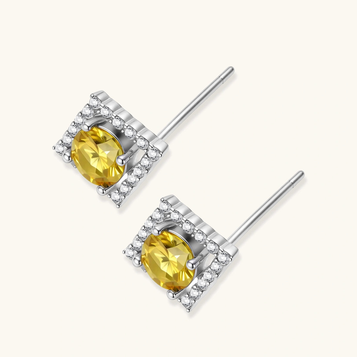 Close-up of diamond-shaped stud earrings with yellow moissanite centers and clear stone halos in sterling silver setting
