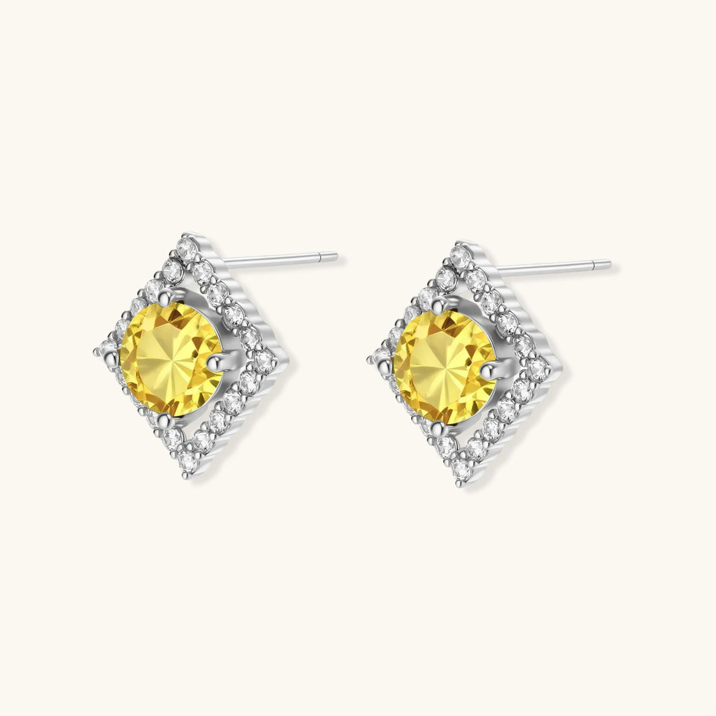 Close-up of diamond-shaped stud earrings with yellow moissanite centers and clear stone halos in sterling silver setting